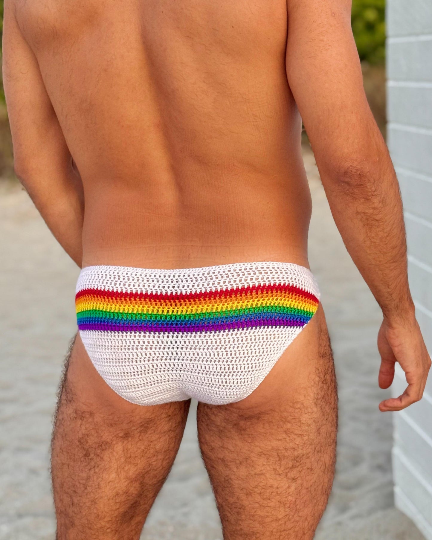 Back view of men’s crochet rainbow swim briefs, highlighting bright stripes and handmade stitch texture.