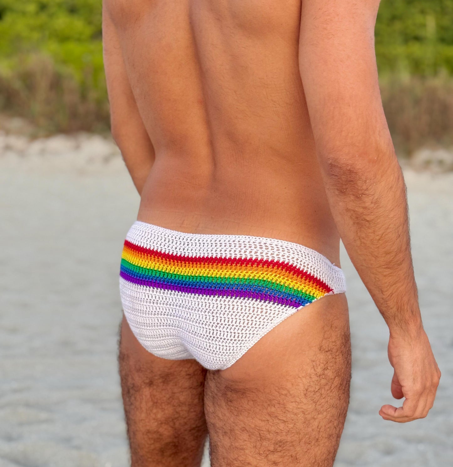 Crochet rainbow LGBTQ men’s briefs on a sandy background, beachwear aesthetic.