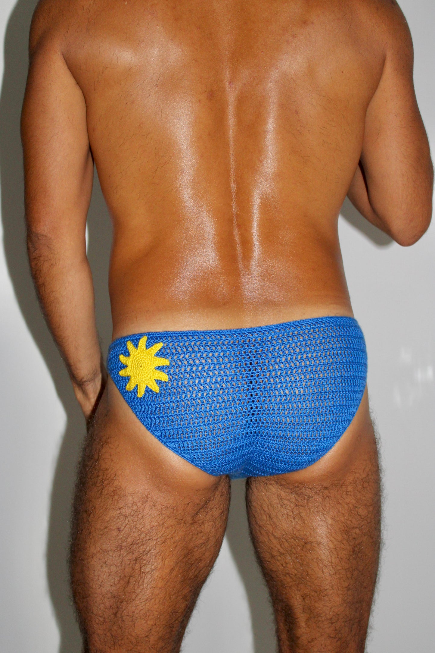 Macro close-up of handmade stitches on crochet men’s swim briefs with yellow sun motif.