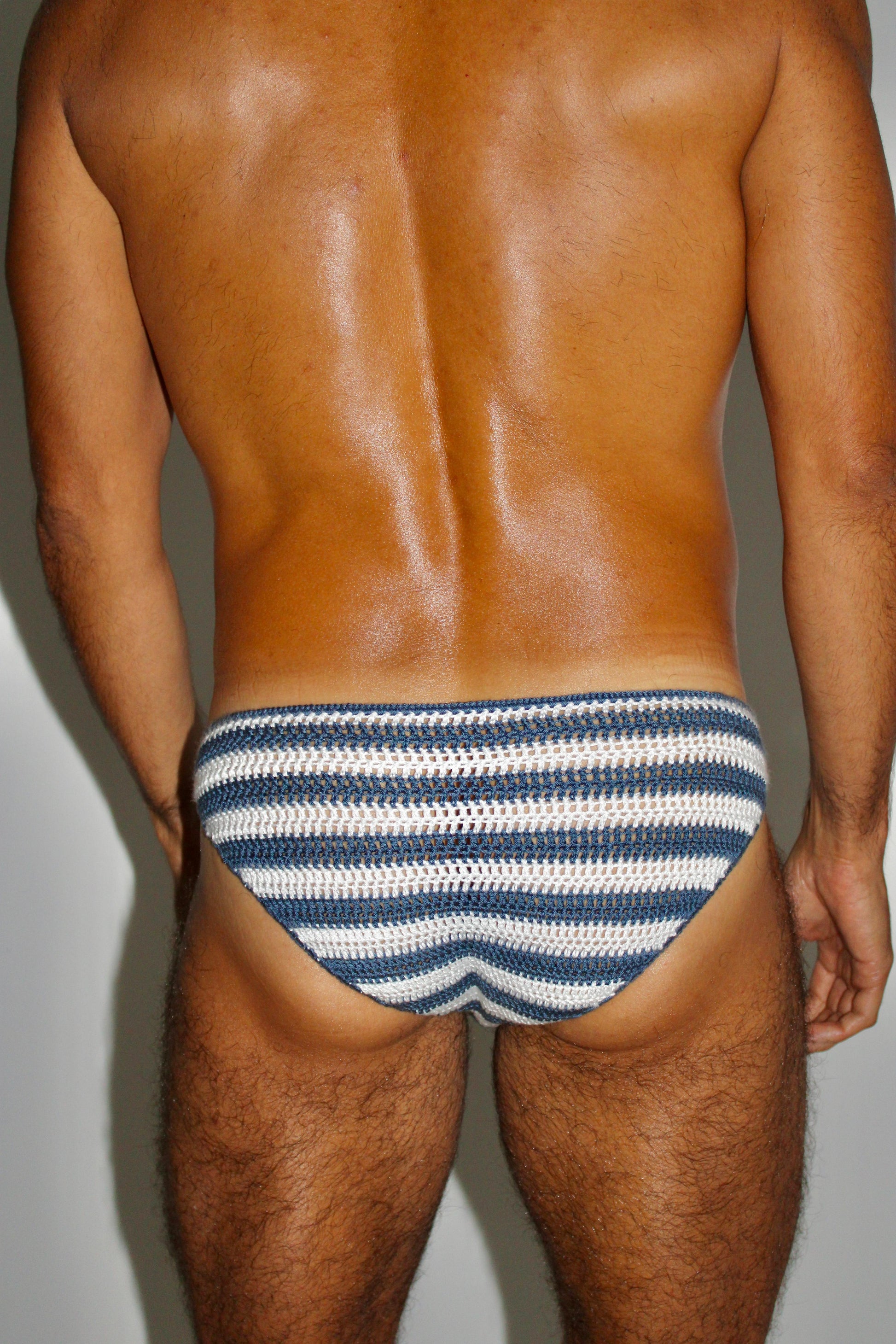 Back angled view of crochet men’s striped swim briefs, showcasing airy structure and snug fit.