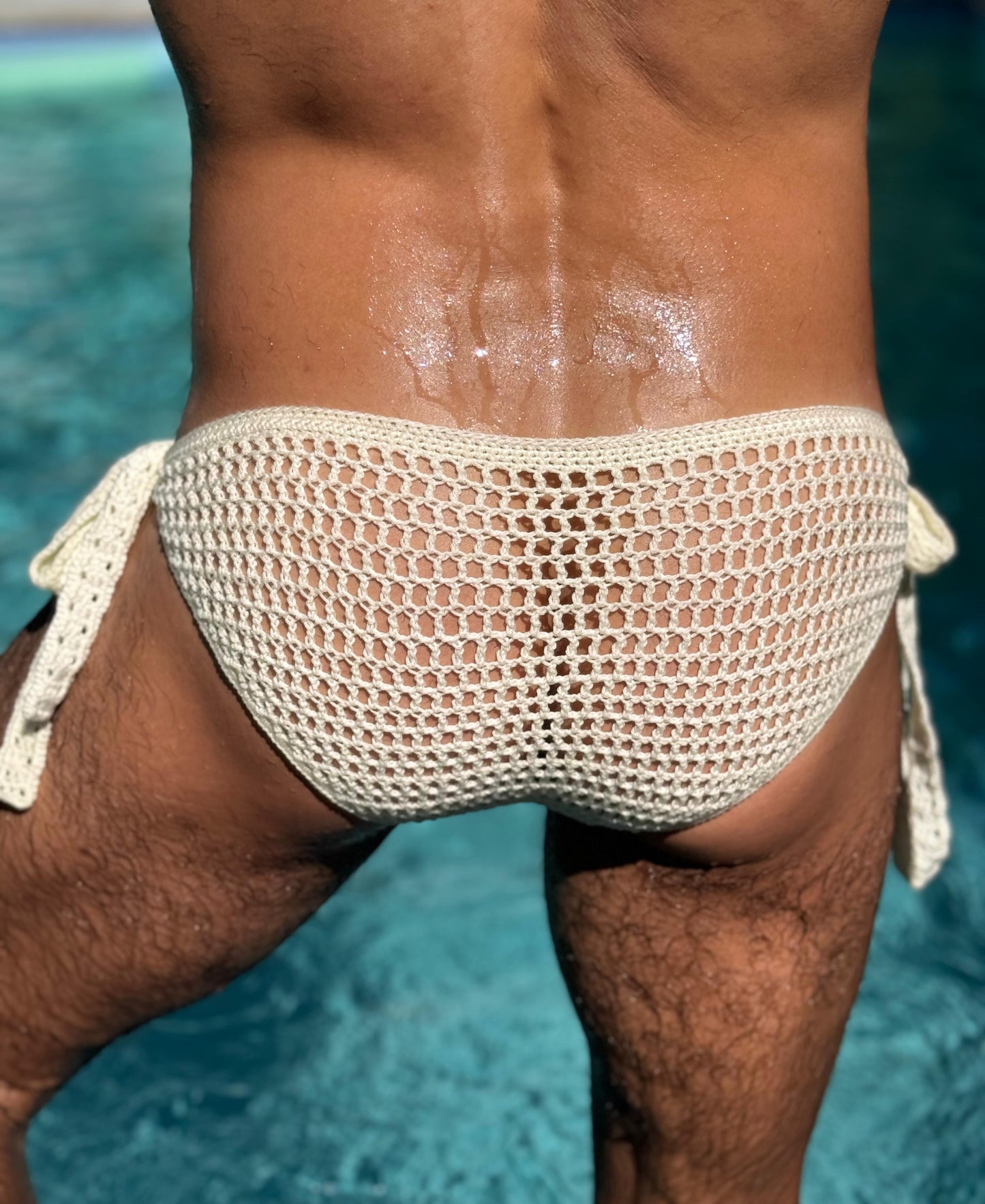 Back view of crochet men’s briefs with side ties near the pool, showing breathable mesh stitch and snug fit.