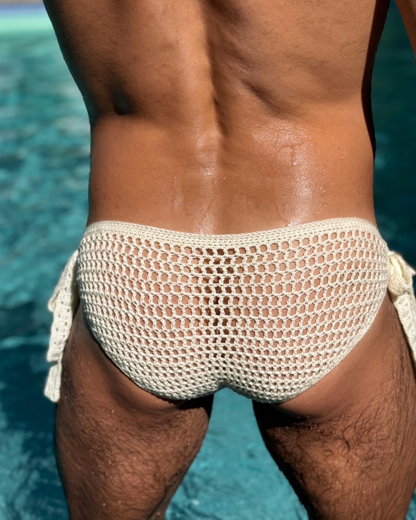 Front view of a man wearing handmade crochet men’s briefs with side ties on the beach, showing fit and breathable design.