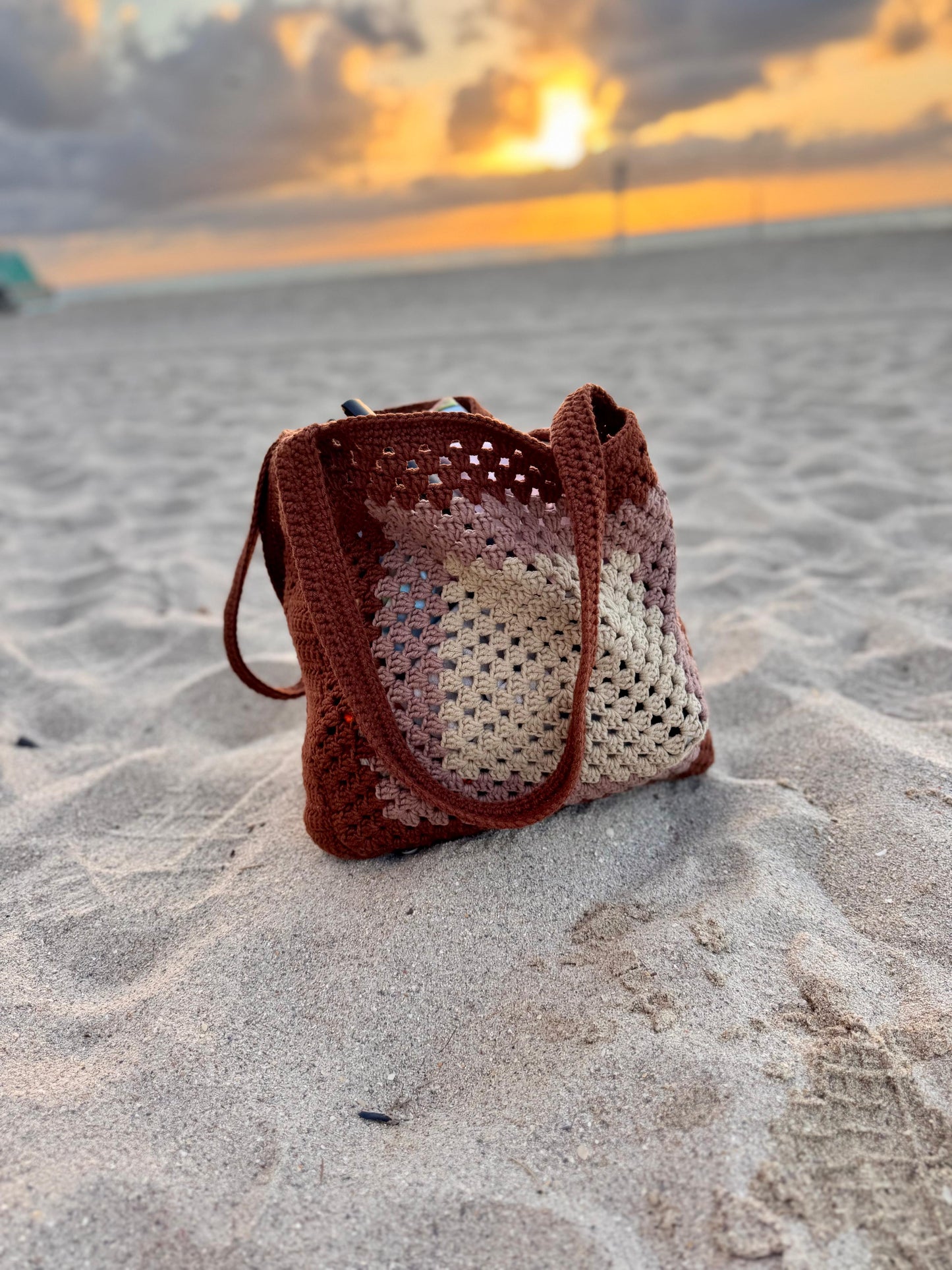 Lifestyle photo of crochet beach tote bag filled with towel and book, styled for summer.