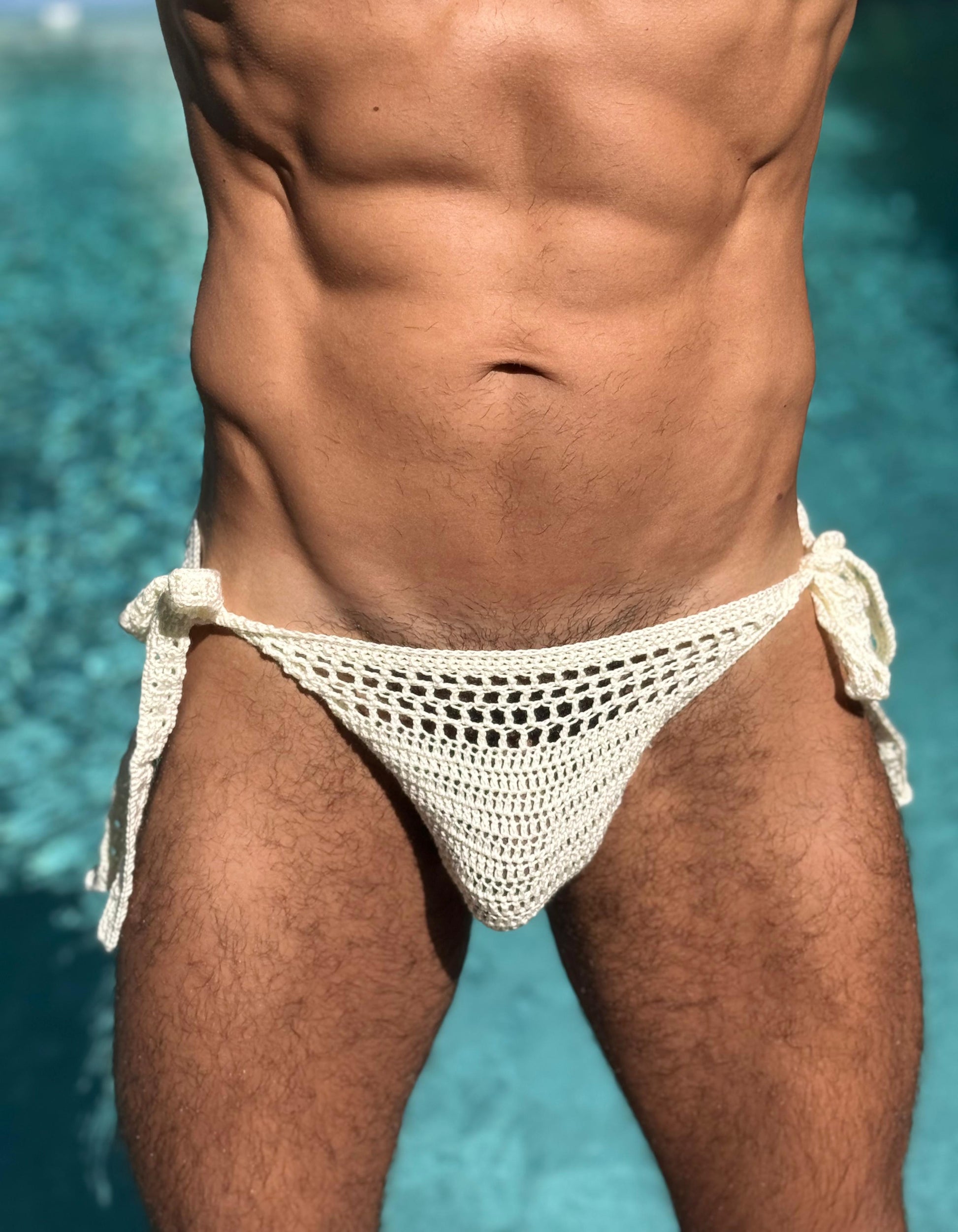 Front view of crochet briefs with side ties against seaside blue, showcasing summer beachwear aesthetic.