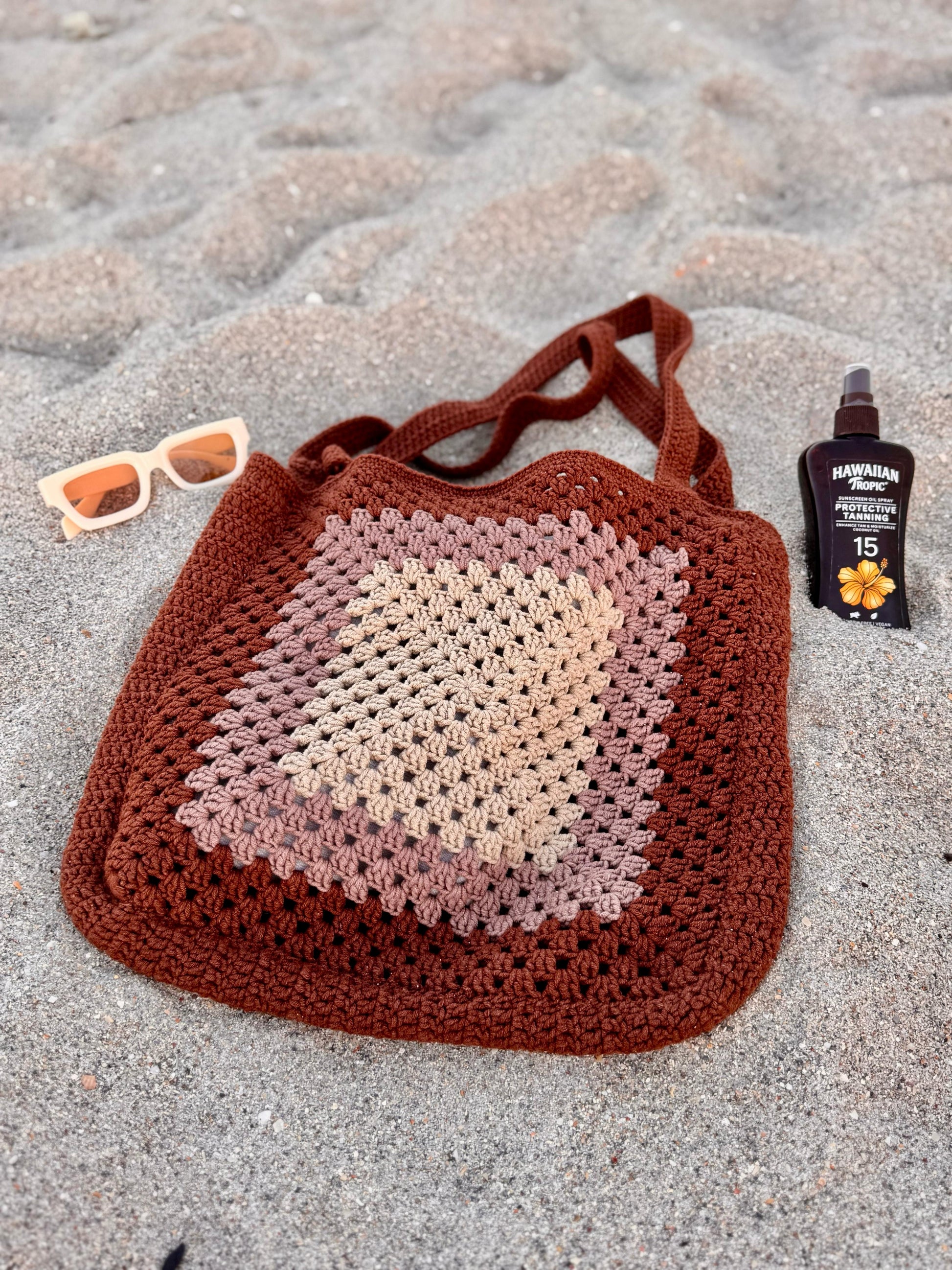 Flat lay of crochet shoulder tote bag with sunglasses and sandscreen, styled for beach essentials.