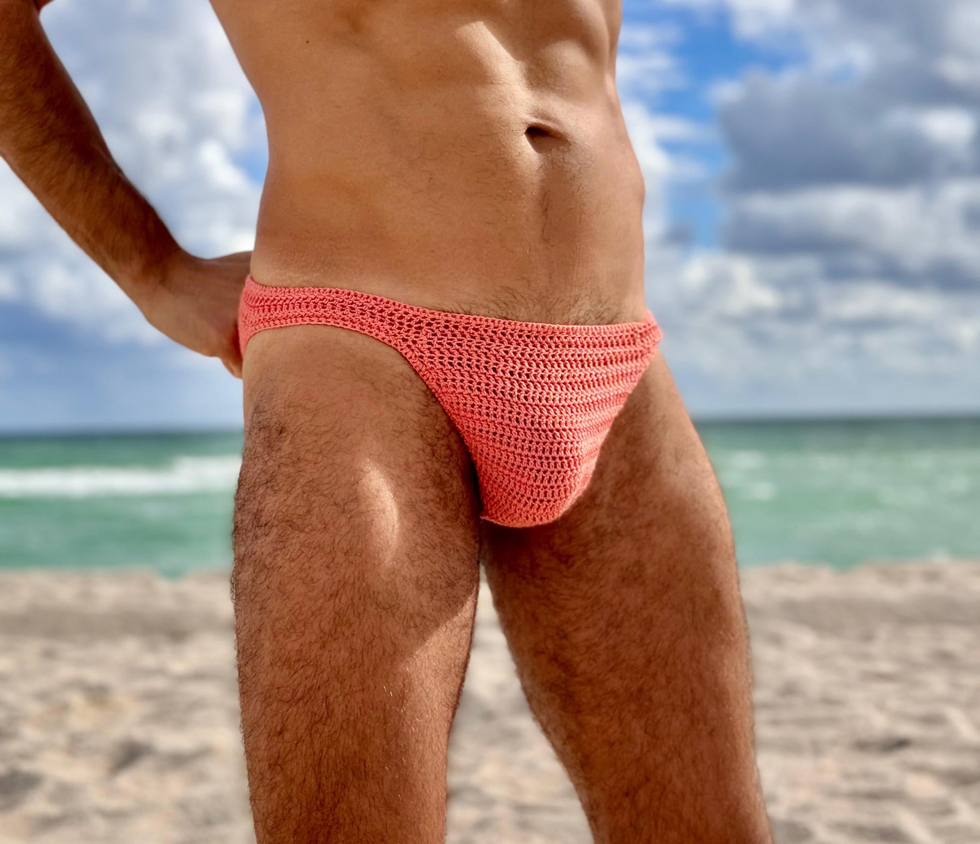 Classic crochet mens swim briefs in coral color side view on beach handmade summer swimwear